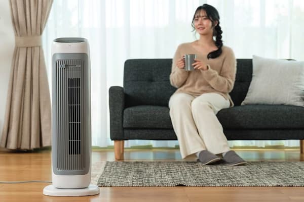 リビングでタワーファンで暖まる女性
