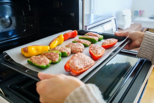 ピーマンの肉詰めをオーブンに入れる女性